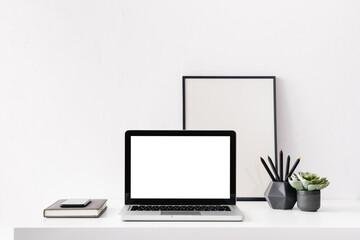 Creative desk with a blank screen, frame or poster, desk objects, office supplies, books, and plant on a white background.	