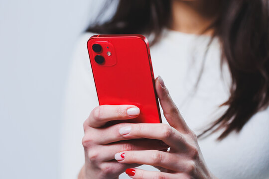 The newest red smartphone in female hands. Woman typing a message on the phone in close-up