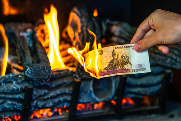 Man's hand holding a one hundred Russian rubles on fire. Currency crisis in Russia. The Russian...