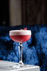 Pink Clover Club Cocktail in Coupe Glass with Layer of Foam and flower Garnish isolated on dark Background
