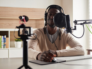 afroamerican  happy young male recording audio blog in headphones microphone broadcasting at home ...