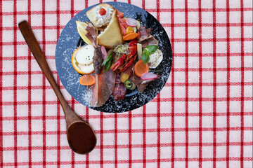 Traditional italien food. Closeup of mixed mediterranean appetizers or antipasto and tapas with ham vegetables and cancer on a black plate and a spoon on red napkin. Topview.