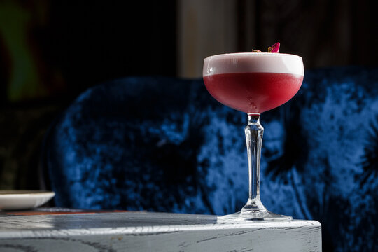 Pink Clover Club Cocktail in Coupe Glass with Layer of Foam and flower Garnish isolated on dark Background