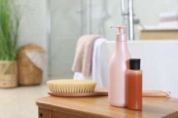 Bottles of shower gels and brush on wooden table near tub in bathroom, space for text