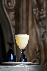 Glass with yellow lemon cocktail decorated with dried lemon chips on the blurred bar counter background.