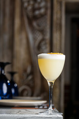 Glass with yellow lemon cocktail decorated with dried lemon chips on the blurred bar counter background.