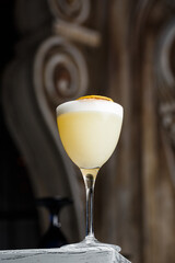 Glass with yellow lemon cocktail decorated with dried lemon chips on the blurred bar counter background.