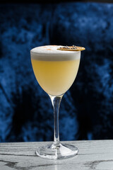 Glass with yellow lemon cocktail decorated with dried lemon chips on the blurred bar counter background.