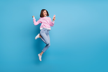 Fototapeta na wymiar Photo of charming lucky lady dressed pink pullover jumping high typing modern device empty space isolated blue color background