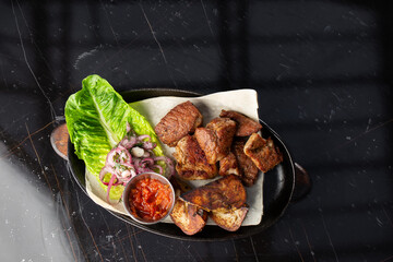 Grilled pork with baked golden potatoes served with red sauce on a dark background. Delicious...