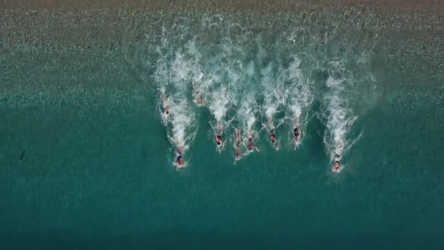 Aerial Shot of Triathlon training on sea shore in the morning. A group of young athletes invades the water. Start swimming in the sea or ocean.