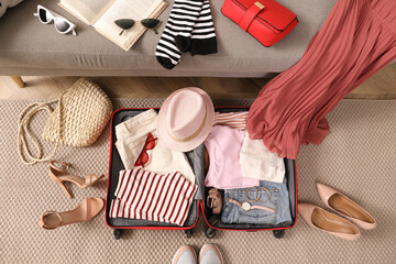 Open suitcase with different women clothes and accessories on floor, top view