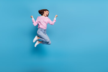 Photo of excited lucky woman wear striped sweater rising fists jumping high empty space isolated blue color background