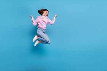 Obraz premium Photo of excited lucky woman wear striped sweater rising fists jumping high empty space isolated blue color background