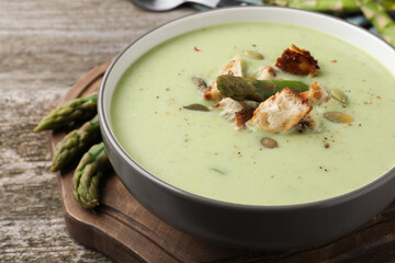 Bowl of delicious asparagus soup on wooden table, closeup