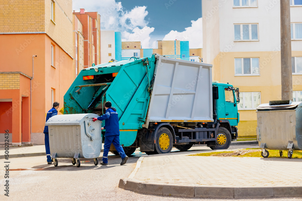 Poster An automobile garbage truck collects garbage in residential areas of a modern city. Men load a metal container with garbage into a car for collecting and transporting garbage.
