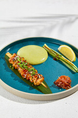 Squid yakitori in ceramic dish on white background. Japanese skewered squid with wasabi sauce. Grilled kalmar on bamboo skewer in asian style. Food menu for izakaya. Summer pan asian menu. © Ryzhkov