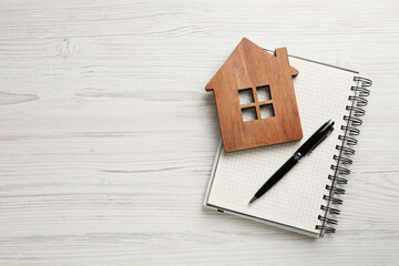 Mortgage concept. House model, notebook and pen on white wooden table, top view with space for text