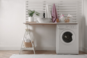 Laundry room interior with modern washing machine and stylish vessel sink on white wooden countertop