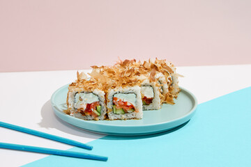 Maki roll with tuna shavings on modern coloured background. Sushi roll with salmon, cheese, cucumber inside, tuna shaving outside. Bonito maki sushi in minimal style. Japanese menu concept.