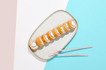 Baked Philadelphia Maki with salmon on ceramic plate. Hot tempura sushi with salmon and philadelphia cheese on coloured background. Japanese menu concept. Hot maki sushi in modern style. © Ryzhkov