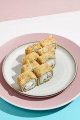 Tempura maki with shrimp on ceramic plate. Hot tempura sushi with shrimp, cucumber and cheese on coloured background. Japanese menu concept. Hot maki sushi in modern style.
