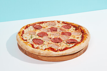 Italian pizza with ham and salami on coloured background. Meat pizza with ham and pepperoni in minimal style on light blue color. American pizza delivery concept with color backdrop