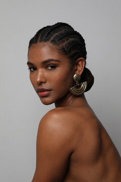 Portrait of African young woman with braids hairstyle posing on grey wall.