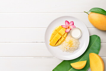 Flat lay of Ripe mango with sticky rice and coconut milk on white wood background.