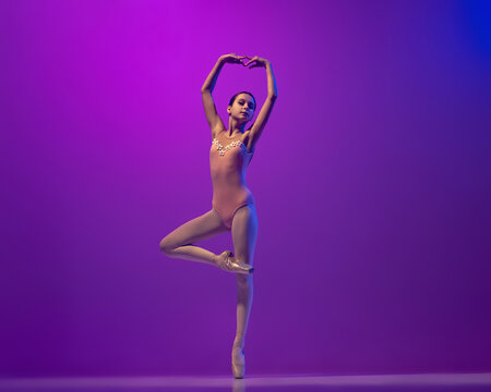 Portrait of young little ballet dancer, teen practicing, dancing isolated on purple background in neon light. Art, grace, beauty, ballet school concept