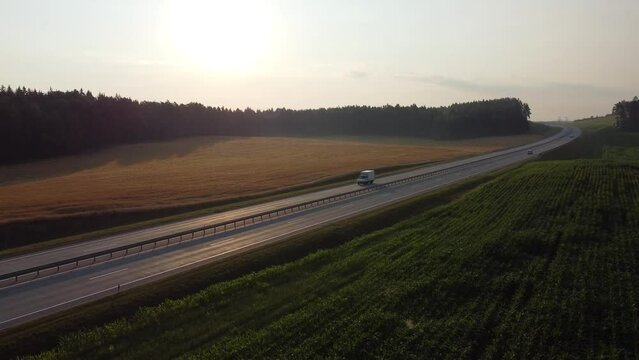 Aerial view of a beautiful country expressway with a small cargo van passing by at dawn. The concept of freight transportation, courier service, long-distance delivery, transport and logistic. High