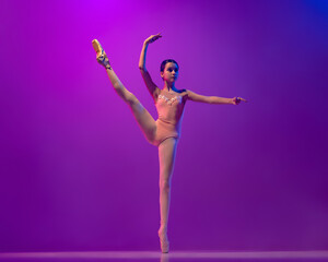 Portrait of young little ballet dancer, teen practicing, dancing isolated on purple background in neon light. Art, grace, beauty, ballet school concept