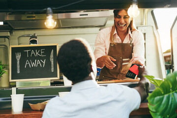 African man making contactless payment with mobile phone at food truck restaurant outdoor - Soft focus on woman chef face