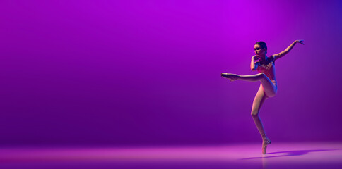 Fototapeta na wymiar Portrait of young little ballet dancer, teen jumping isolated on purple background in neon light. Art, grace, beauty, ballet school concept