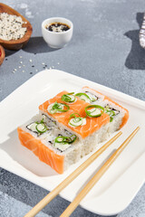 Maki roll with salmon and wasabi sauce on white plate in contemporary composition. Sushi roll with chopsticks on concrete table. Maki sushi philadelphia in minimal style.
