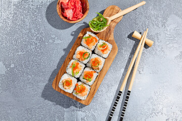 Maki roll with salmon tartare top and tobiko on wooden board in contemporary composition. Sushi roll with chopsticks on concrete table. Maki sushi in minimal style.