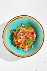 Stir fry noodles with chicken and bacon in asian style. Fried udon with meat and vegetables in ceramic bowl on white background and sunlights shadows. Asian food in modern style.
