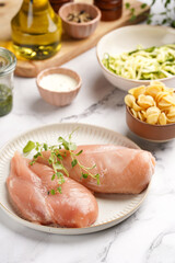 Fresh ingredients for preparing a warm salad on marble surface: chicken breasts, heavy cream, zucchini noodles, italian pasta orecchiette, herbs and sauces