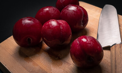 Red plums on bread board with knife and black background
