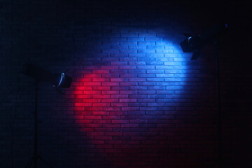 Bright blue and red spotlights near brick wall in dark room, space for text