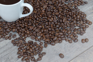 Coffee beans scattered on the table diagonally and a white cup of coffee.
