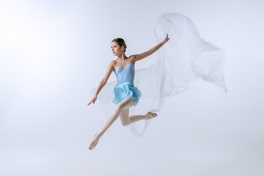 One young girl, aspiring ballerina in blue dress and pointes dancing with cloth isolated on gray background. Art, grace, beauty, ballet school concept