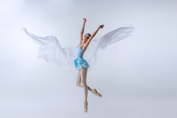 One young girl, aspiring ballerina in blue dress and pointes dancing with cloth isolated on gray...