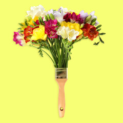 Creative design with paint brush and beautiful freesia flowers on yellow background. Spring is coming