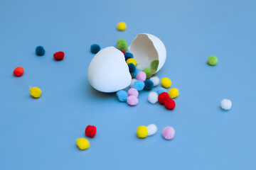 Cracked white egg with multi-colored round pom-poms falling out of it on a blue background