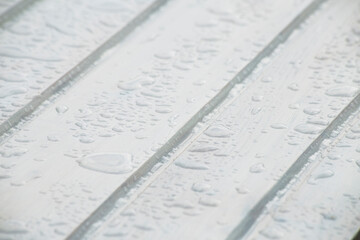 white wooden plank surface in diagonal position with raindrops. selective spotlight copies space. background for invitation.