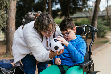 Child with multiple disabilities in a wheelchair playing with a soccer ball with her mother...