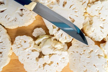 Fototapeta na wymiar Man cuts raw cauliflower steaks on a wooden cutting board. Preparation for cooking. Vegetarian food.