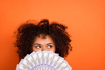 Portrait of attractive trendy funny mysterious girl holding cash hiding face isolated over bright orange color background