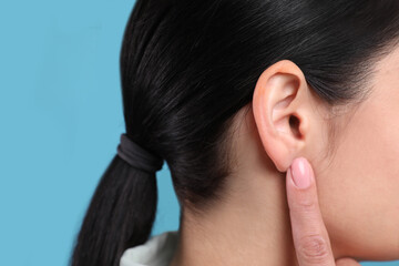 Woman pointing at her ear on light blue background, closeup